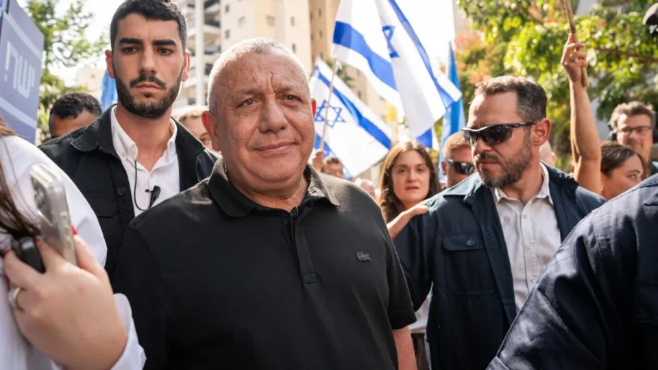 Gadi Eisenkot in a black polo shirt walking through a crowd of supporters waving Israeli flags at a polling station in Holon.